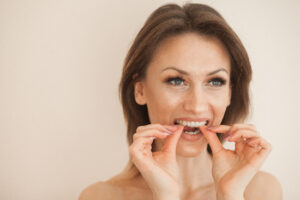 head shot of a woman putting in her clear aligner against a beige background